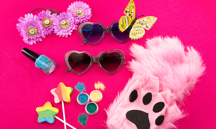 Two pairs of heart-shaped sunglasses, flower headbands, butterfly hair clip, pink paw glove, glitter, lollipops, and nail polish.