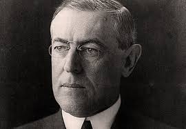 Black and white portrait of a man with short hair, glasses, and a serious expression, wearing a suit and tie.