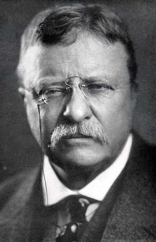 Man with round glasses and a mustache, wearing a suit and tie.