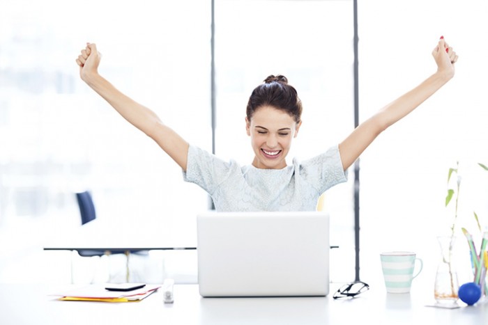 Person celebrating with arms raised in front of a laptop, expressing joy and success.