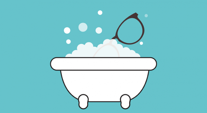 Bathtub filled with bubbles and a pair of glasses resting on top.
