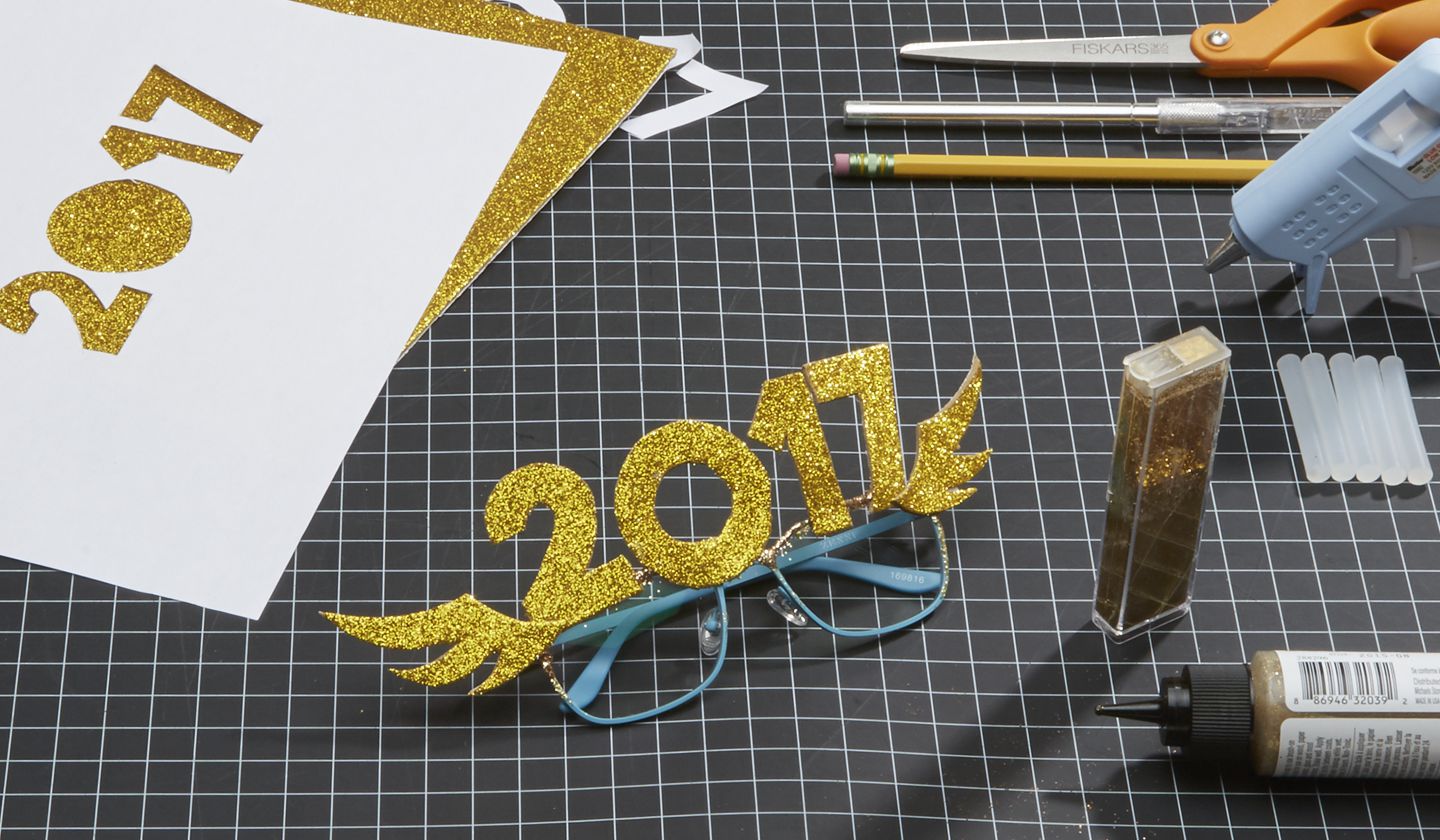 Glittery gold &quot;2017&quot; on blue glasses, craft tools and materials around.