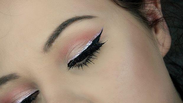 Closed eye showcasing pink eyeshadow, black eyeliner with a silver streak above it, and long mascara-coated lashes.