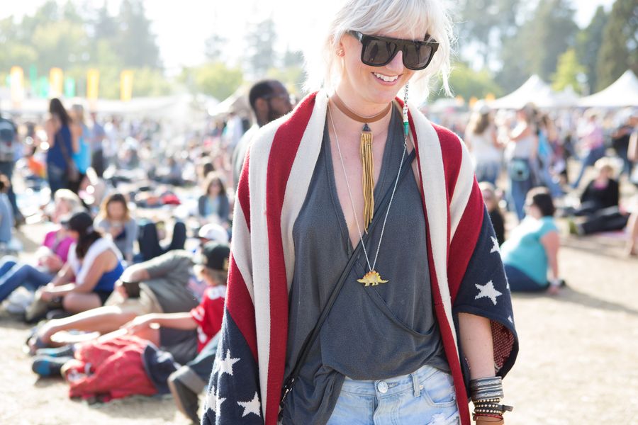 Woman wearing a flag-themed sweater, a gray top, distressed denim shorts, and a gold dinosaur necklace.
