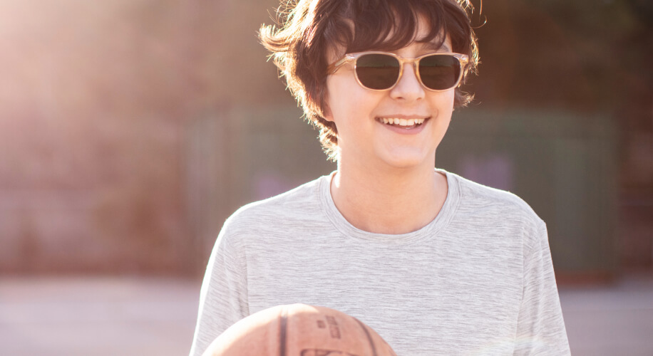 Young boy wears sunglasses while playing basketball.