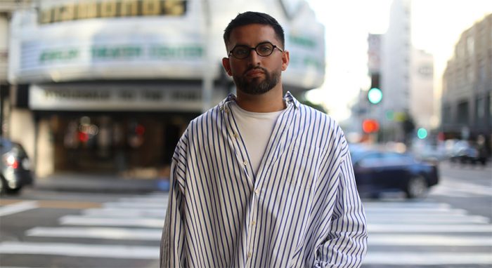 Man wearing oversized striped shirt and glasses standing on city street.