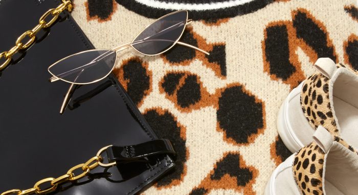 Black purse with a gold chain, cat-eye sunglasses, and leopard-patterned shoes on a leopard-print rug.