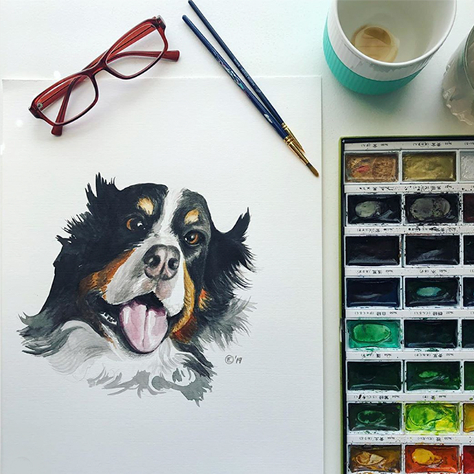 Watercolor painting of a dog’s happy face, next to paintbrushes and a watercolor palette.