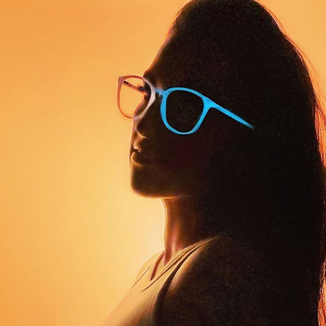 Person wearing neon blue and orange glasses against an orange gradient background.