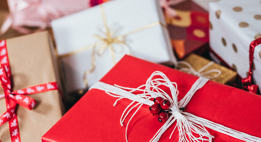 Colorful wrapped presents with various ribbons and bows, featuring one red gift with white string and red berries.