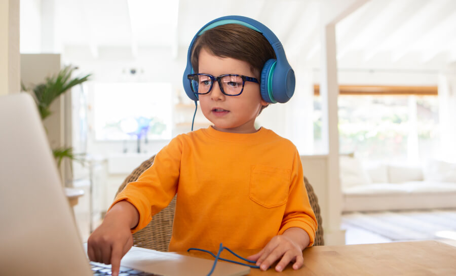 Young child wearing blue headphones and orange shirt, using a laptop.
