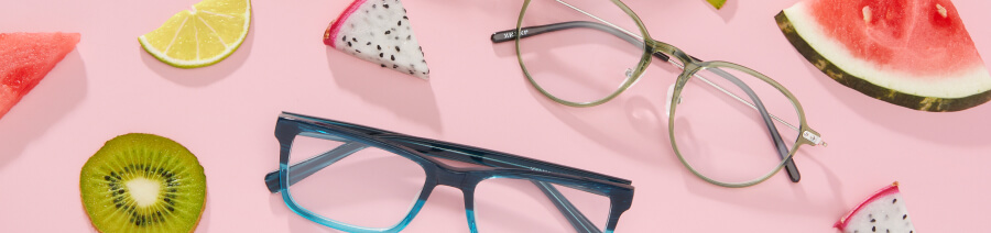 Two pairs of Zenni glasses sit on a pink background surrounded by slices of dragon fruit, watermelon, kiwi, limes, and lemons.