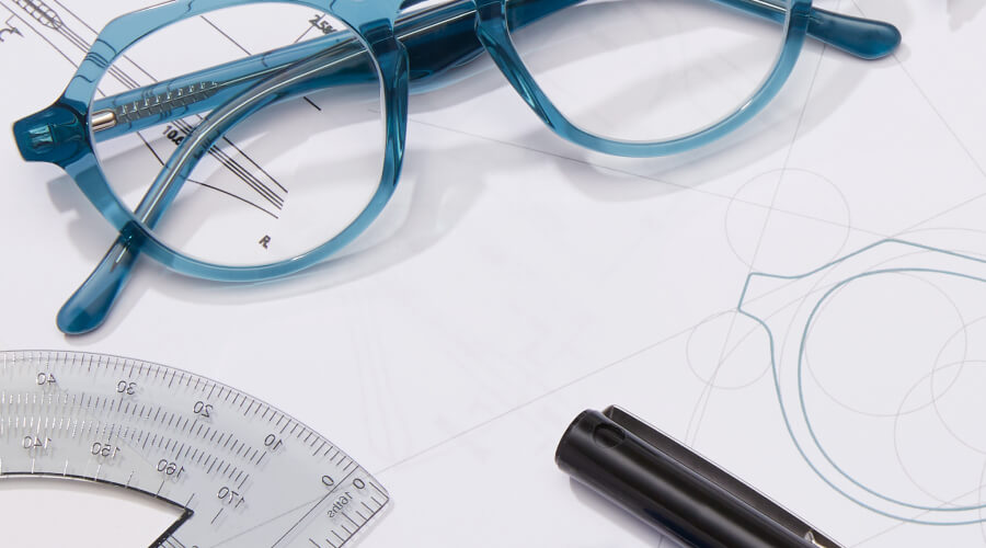 Blue Zenni eyeglasses sit on a drawing table with rulers, pens, and pencils.