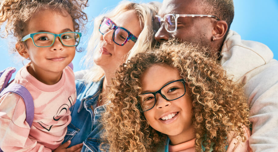 Family of two adults and two children smile and embrace while wearing Zenni glasses.