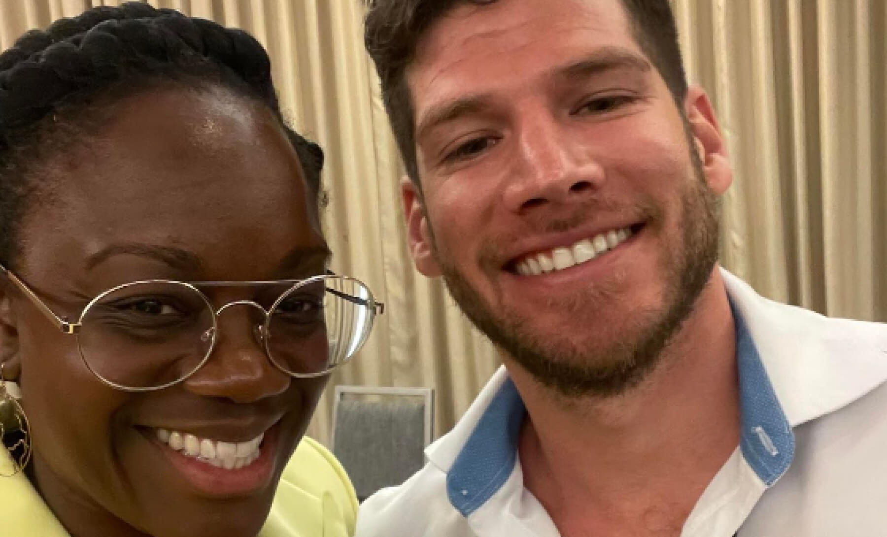 Two people smiling; one wearing glasses and a yellow shirt, and the other in a white shirt with a blue collar.