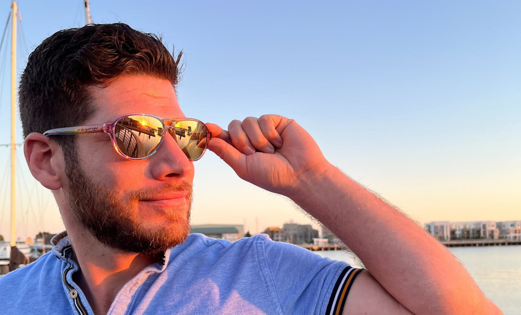 Man adjusting his reflective sunglasses showing a sunset.