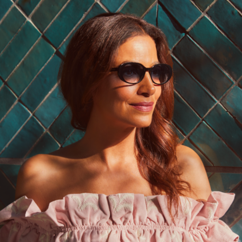 Woman wearing dark sunglasses and a pink off-shoulder top with ruffled details.