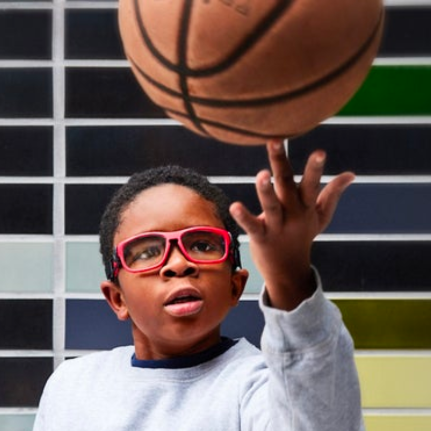 Child wearing red glasses, gray sweatshirt, spinning a basketball on fingertip.
