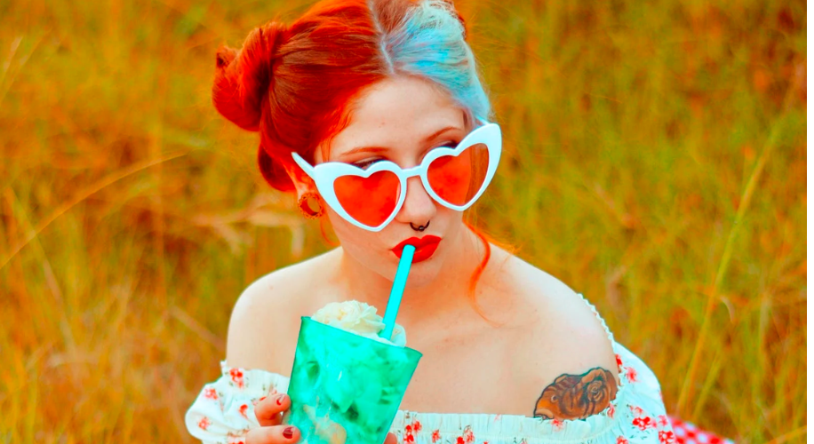 Woman with heart-shaped sunglasses drinking from a turquoise cup with a blue straw.