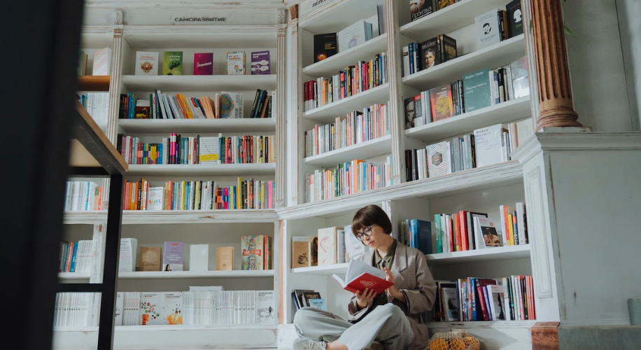Person reading a book titled &quot;Design&quot; in a cozy library filled with various genres of books.