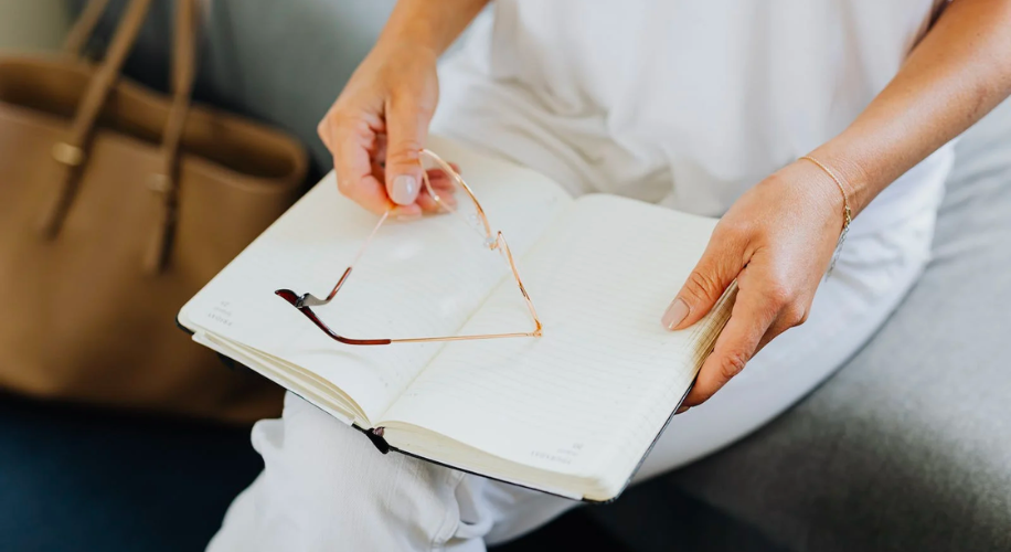 Hands holding glasses over an open notebook without any visible text.