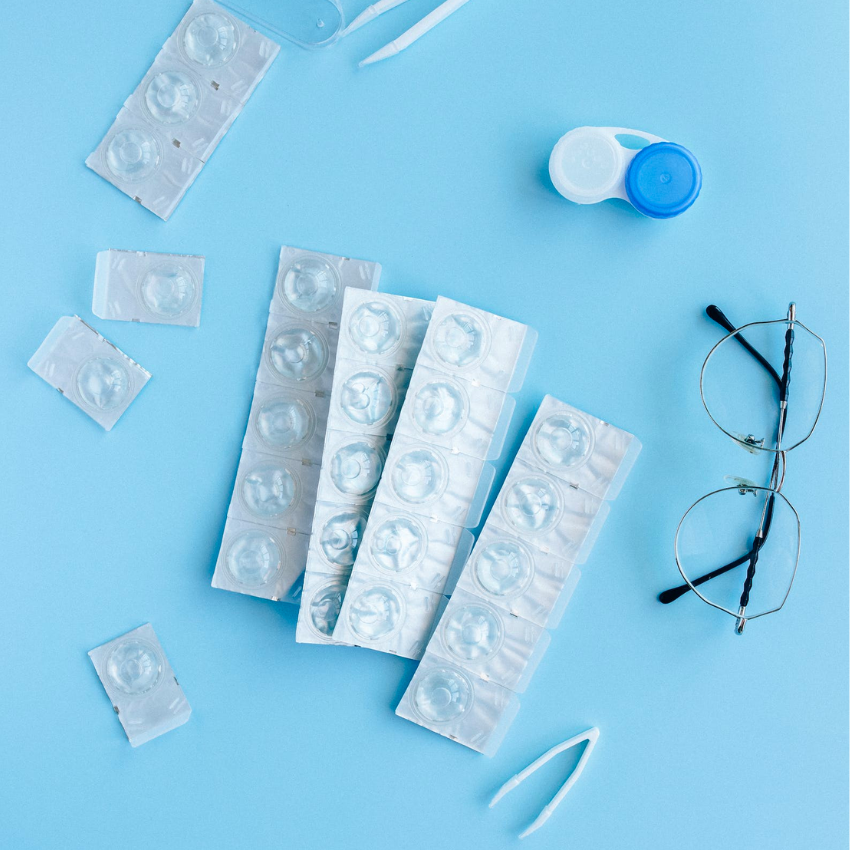 Contact lens blister packs, contact lens case, tweezers, and eyeglasses on a blue background.