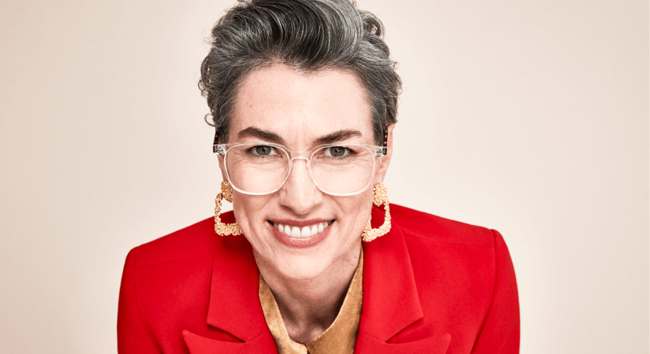 Woman wearing glasses with a red blazer and gold earrings, smiling at the camera.
