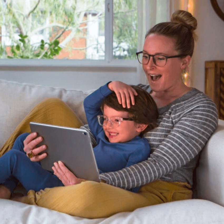 Woman and child smiling at a tablet screen while sitting on a white couch.