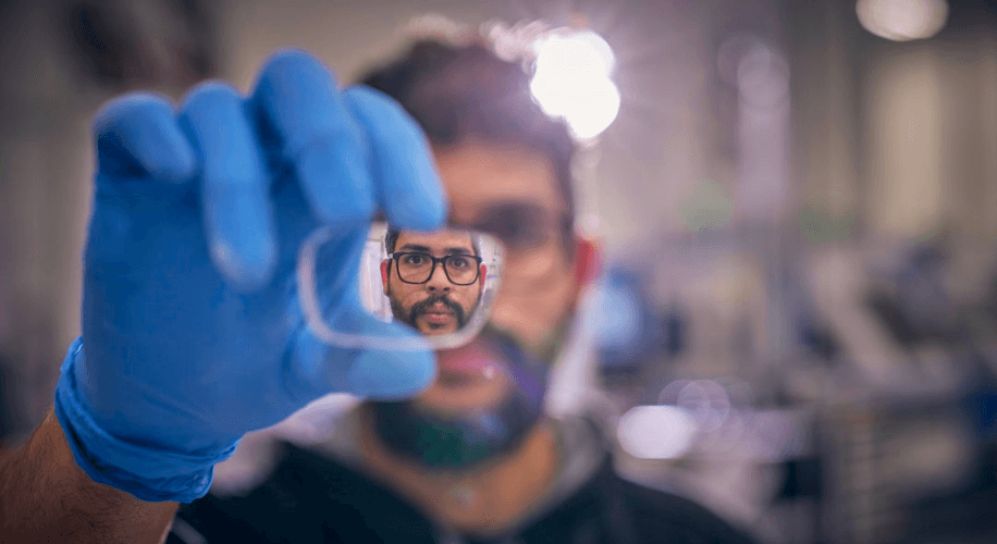 Blue gloved hand holding a clear lens with a man&#039;s face seen through the lens.