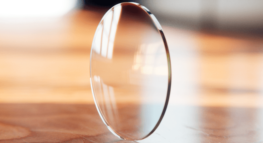 Thin, circular transparent lens standing upright on a wooden surface.