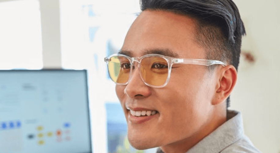 Man wearing clear glasses with amber-tinted lenses, smiling.