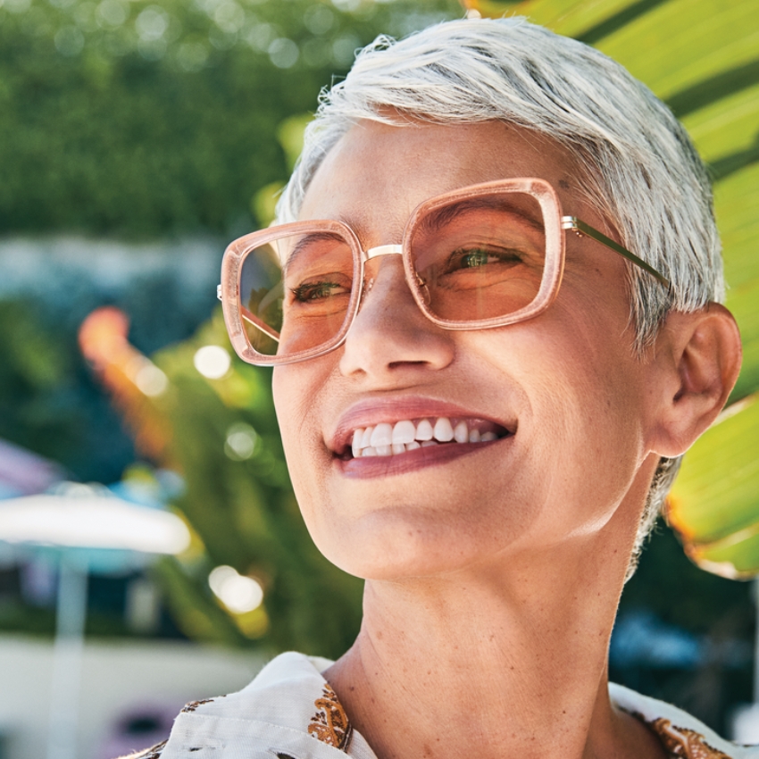 Woman wearing oversized pink sunglasses with square frames and a confident smile.