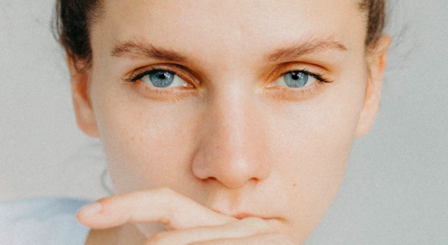 Close-up of a person with blue eyes, gazing intently, with hand partially covering their mouth.
