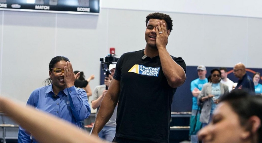 Two people smiling while covering their right eyes, one wearing an Armstead Academic Project T-shirt.
