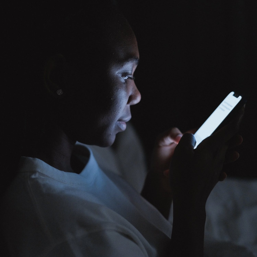 Person using a smartphone in a dimly lit environment with the screen illuminating their face.