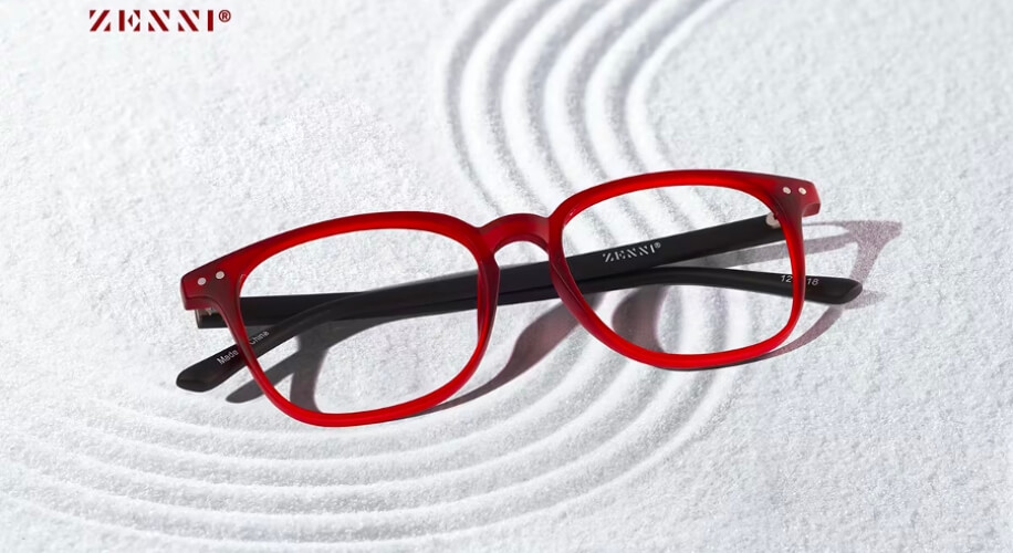 Red Zenni eyeglasses with black temples on a textured white surface; Zenni logo on the temples.