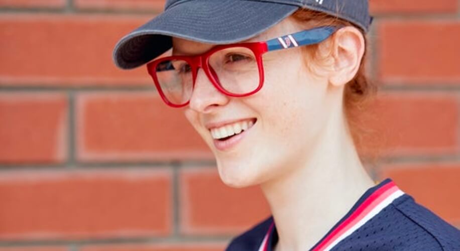 Person wearing a navy blue cap, red-framed glasses, and a navy blue jersey with red and white accents.