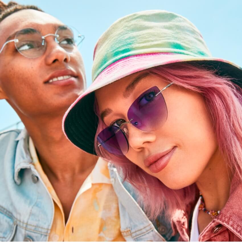 Two people wearing colorful sunglasses; one wears a bucket hat, and both have trendy, casual outfits.