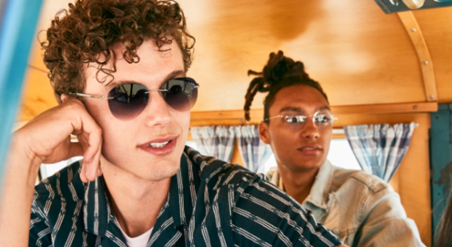 Two individuals wearing sunglasses, seated in a wooden interior with checkered curtains.
