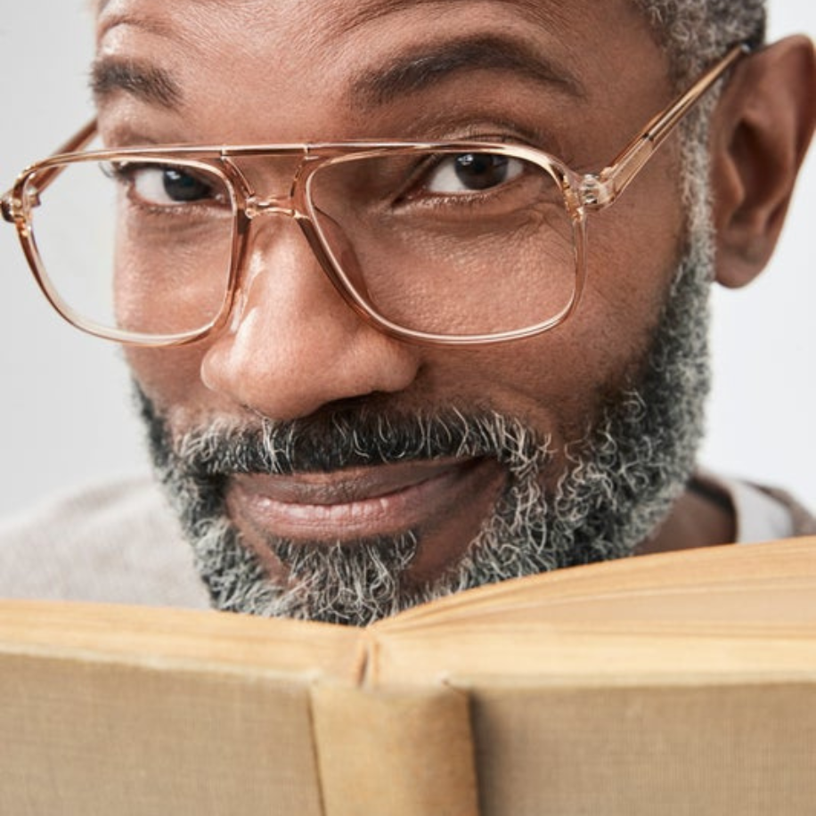 Man wearing large, gold-framed glasses while reading a book.