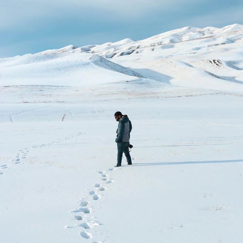 Person wearing a blue jacket and jeans, walking through a snowy landscape, leaving footprints behind.