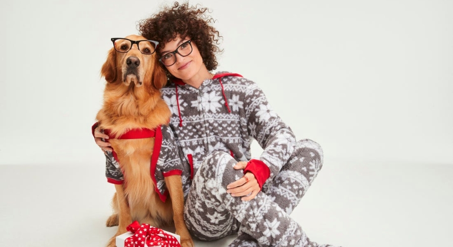 Dog and person both wearing matching gray, white, and red snowflake-pattern pajamas.