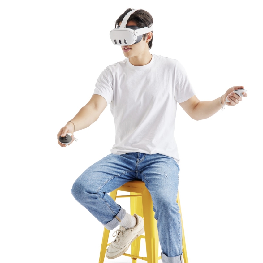 Person using a VR headset and holding controllers, seated on a yellow stool.