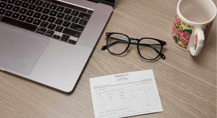 Laptop, black-framed eyeglasses, a floral-patterned mug, and prescription card text: &quot;JOHN DOE, O.D.&quot;