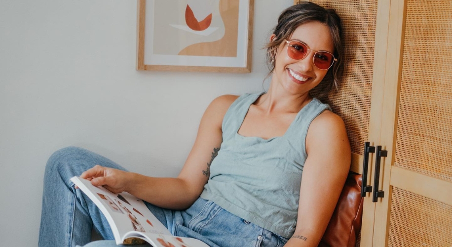 Woman wearing sunglasses and a tank top, smiling while reading a magazine.