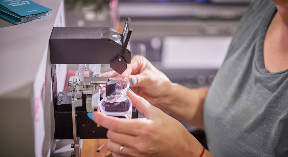 Optician adjusting eyeglass lenses with a machine for precise fitting.