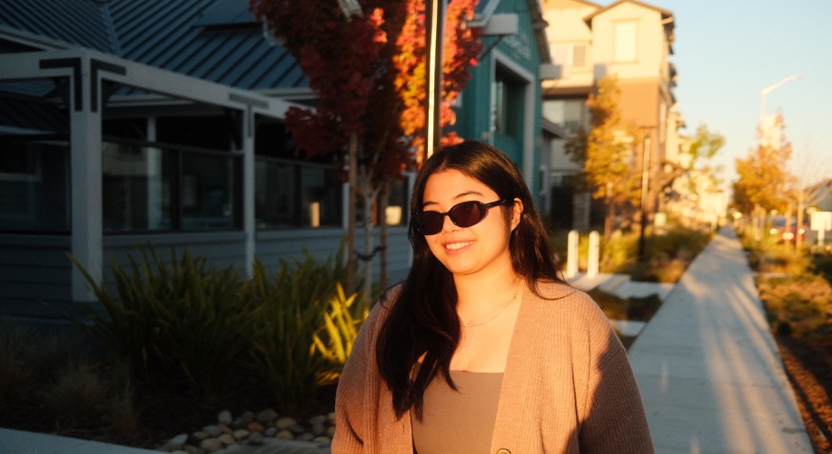 Woman wearing sunglasses and a brown cardigan smiling outdoors.