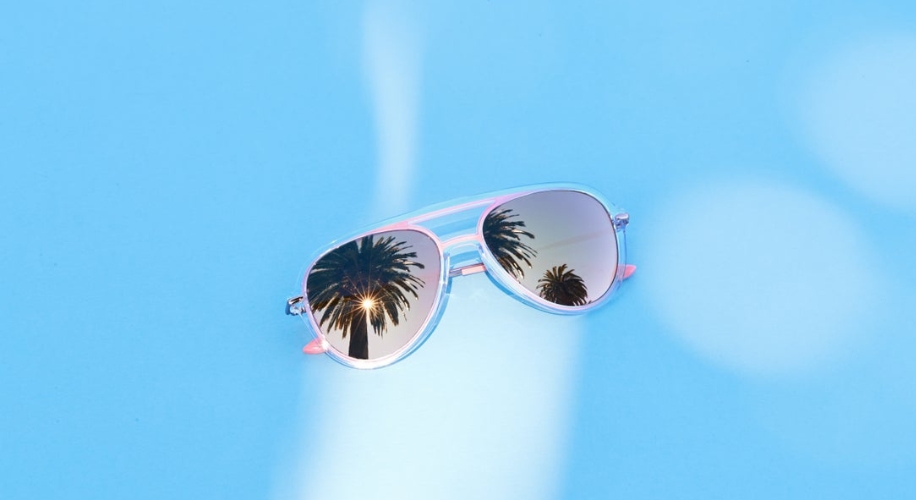 Aviator sunglasses reflecting palm trees on a light blue background.