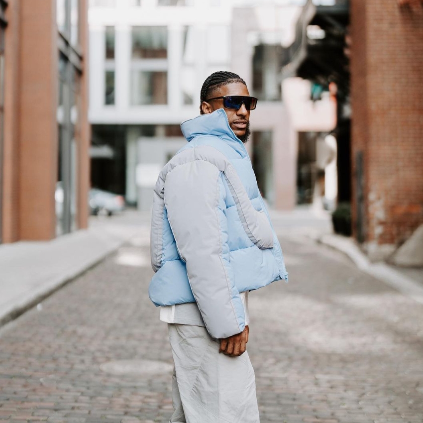 Man wearing a light blue and gray puffer jacket and gray pants, standing in a cobblestone street.