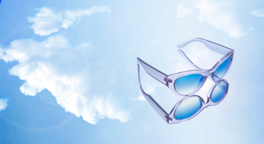 Blue-lensed sunglasses with translucent frames reflecting against a cloudy sky background.